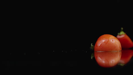 Saftige-Rote-Tomatenscheiben-Fallen-In-4-Teile-Glas-Mit-Wasserspritzern-In-Zeitlupe-Auf-Dunklem-Hintergrund